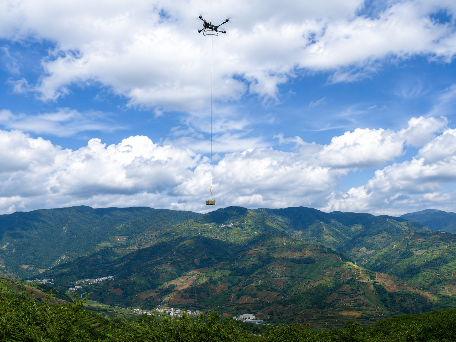 Drone agrícola içando carga sobre região montanhosa